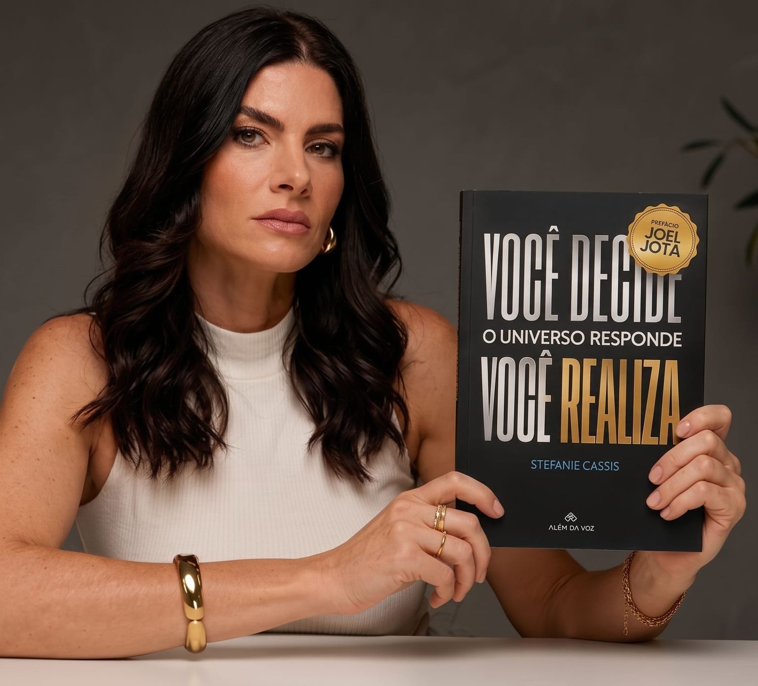Stéfanie Càssis segurando o livro Você Decide. O Universo Responde. Você Realiza.