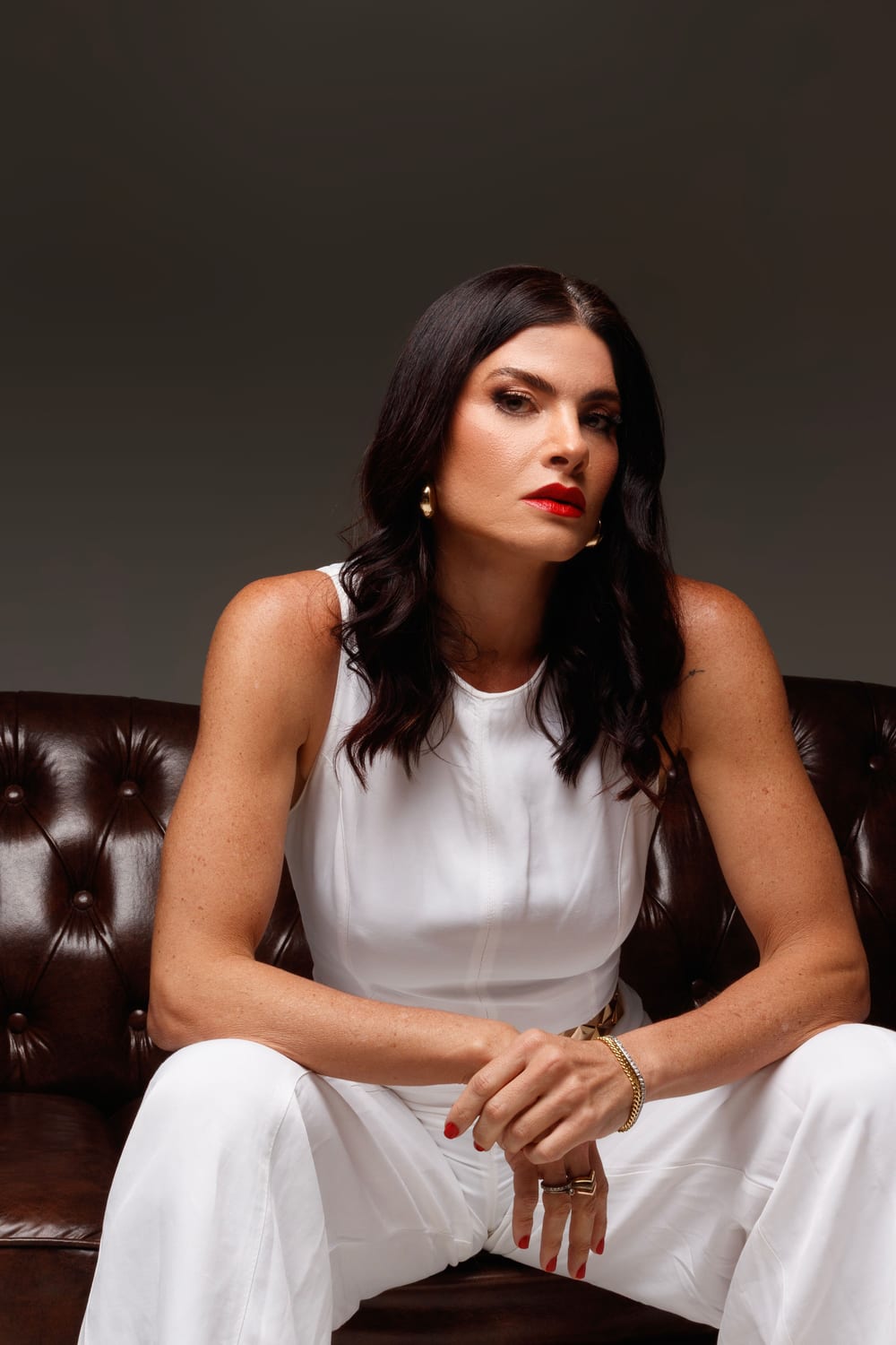 Stéfanie Càssis de branco, sentada num sofá de couro